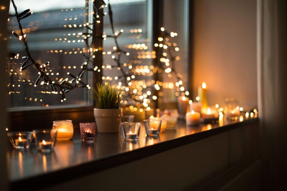 candles burning on window sill with garland lights christmas