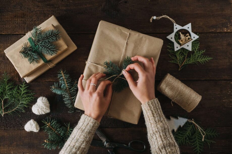 Christmas wrapping idea, xmas wrapping workspace. Female hands wrap gift box in kraft recycled paper. Eco-Friendly, Sustainable, zero waste, natural color Christmas gift boxes on wooden background. Christmas gifts